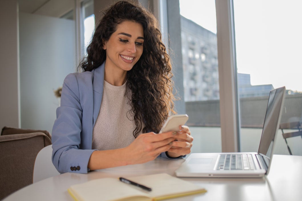 girl smiling in front of her phone and laptop